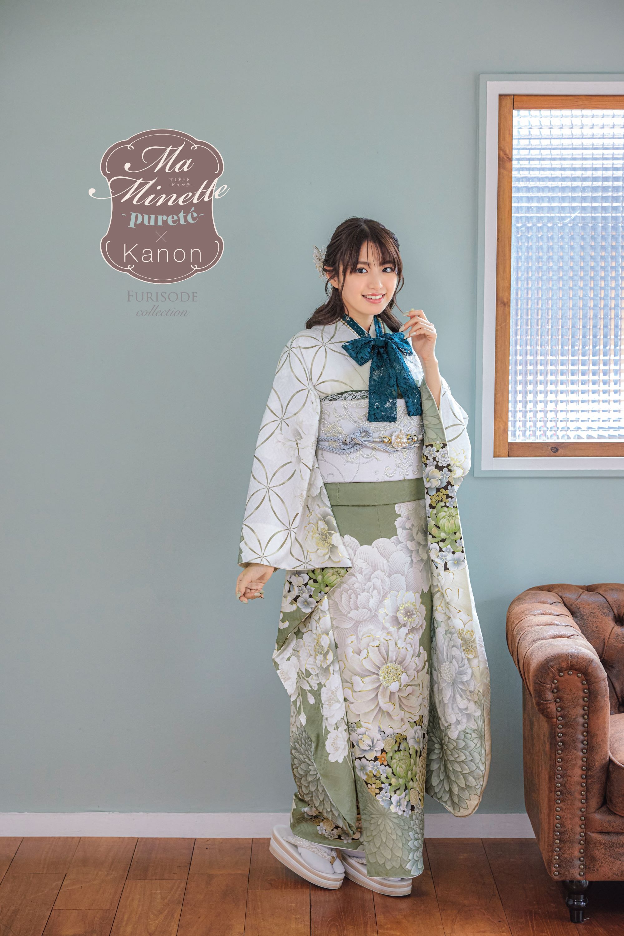 パステル グリーンと白の花柄の着物を着た女性が、水色の壁の部屋に立っています。彼女は左手で着物の端を持ち、微笑んでいます。彼女の右側には茶色のソファが部分的に見えます。上部には、エレガントな筆記体で「Ma Minette pureté Kanon 振袖コレクション」と書かれています。