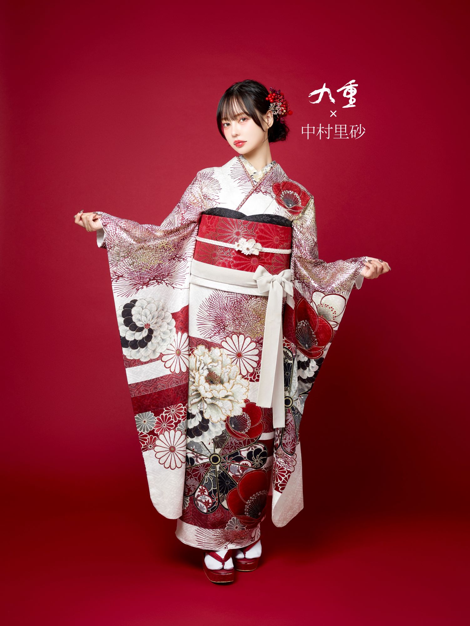深紅の背景に、赤、黒、白の花柄があしらわれた華やかな着物を着た女性が立っています。髪には赤い花を挿し、着物の袖を広げています。伝統的な白いソックスとサンダルを履き、自信に満ちた表情で立っています。彼女の横にテキストが表示されます。.