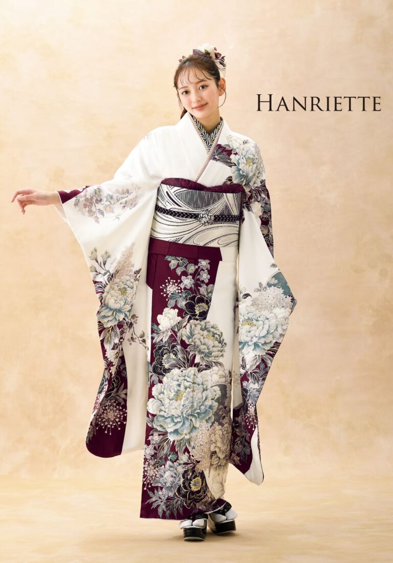白、ワインレッド、ラベンダーの色合いの豊かな花柄の伝統的な着物を着た女性が立っています。彼女の髪は、それに合わせたアクセサリーでエレガントにスタイリングされています。背景は柔らかく、ニュートラルな色調です。右上隅に「Hanriette」という文字が印刷されています。.