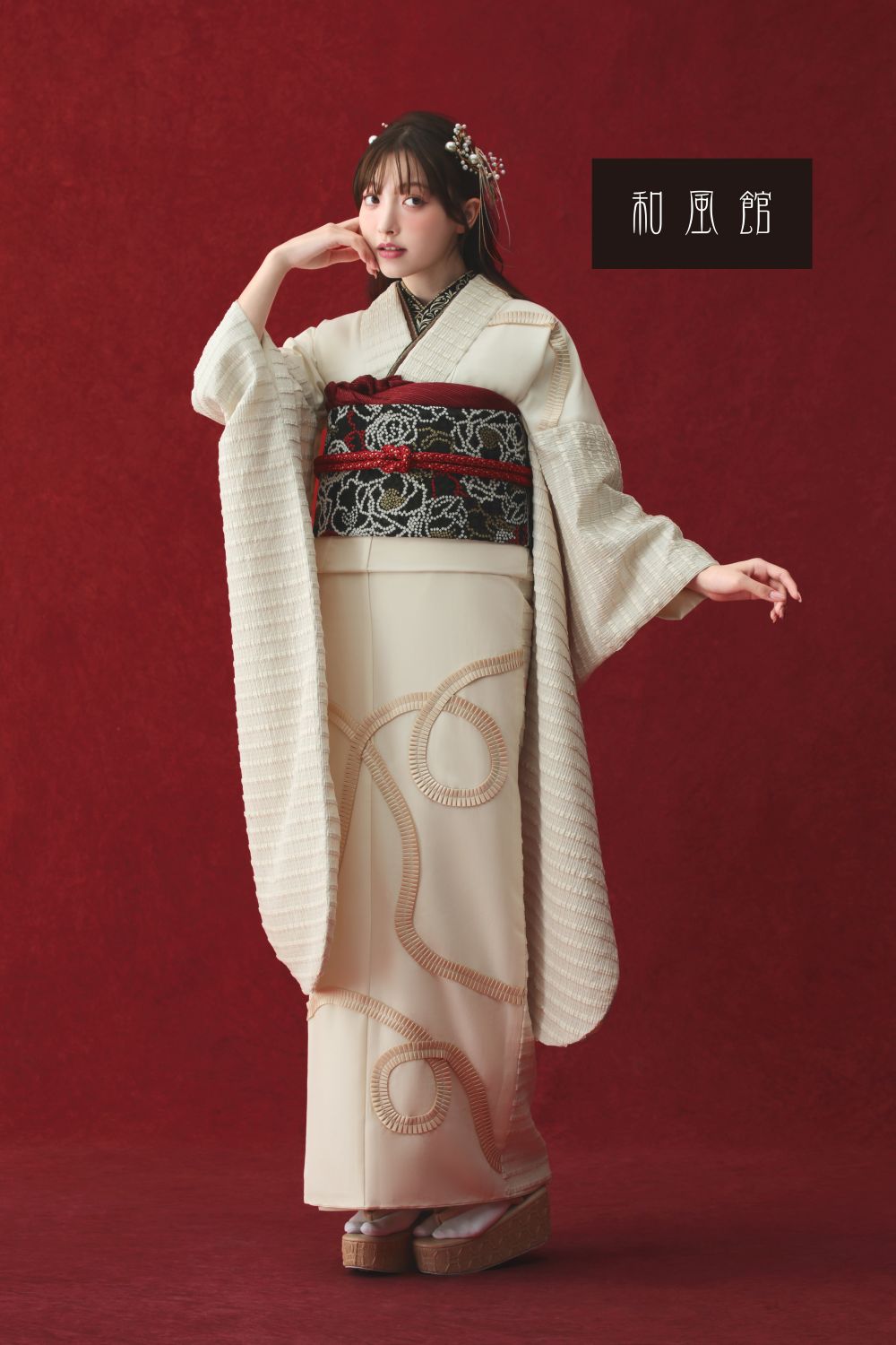 この人物は、黒と赤の刺繍が施された伝統的な白い着物、製品番号 25WF11 を着て、ヘアスタイルを整え、アクセサリーを身に着け、深紅の背景に立っています。木製のサンダルを履いて、片手を顔の近くに置いたポーズで、このルックを完成させています。右上隅に日本語のテキスト ボックスが表示されています。.