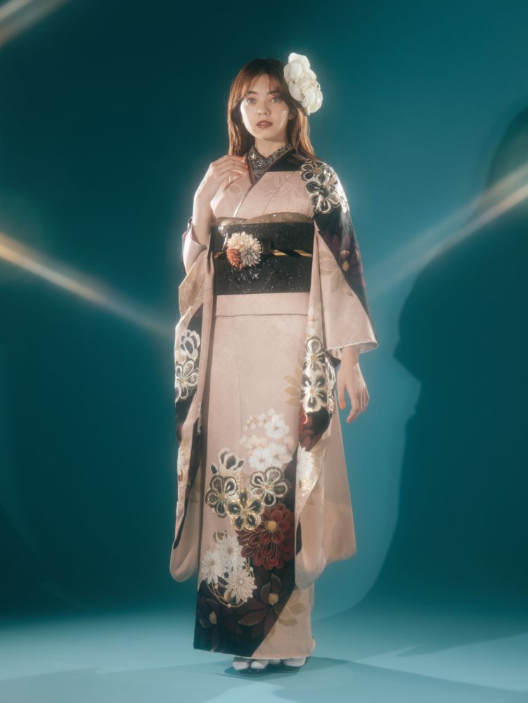 ピンクと黒の花柄の着物を着た女性が、青緑色の背景に立っています。彼女の手は優しく襟に触れています。髪には白い花が飾られています。照明が彼女の周囲に柔らかな光を放ち、背景に彼女の影が映っています。.